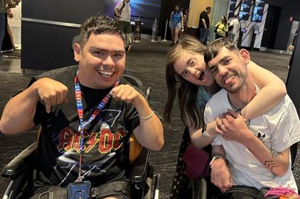 Three people smiling together at an event, one using a wheelchair